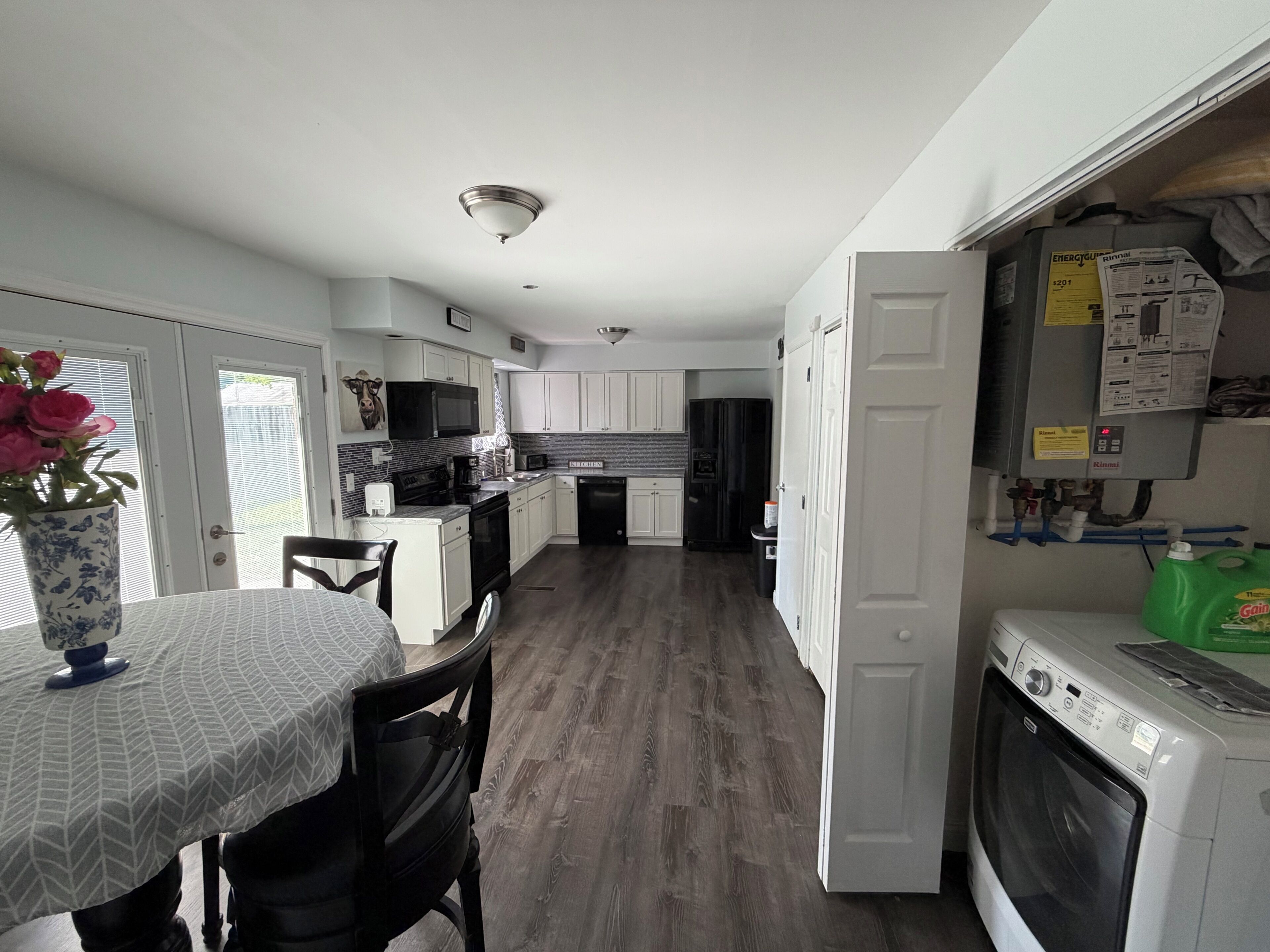 Una cocina con gabinetes blancos, una mesa de comedor con sillas, un refrigerador y una lavadora.