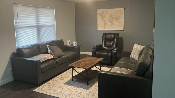A living room with a black leather sofa, a leather recliner, a wooden coffee table, and a world map on the wall. - PERFECT MIAMI STAY 4-bedroom 2 bath with luxury shower in O (Oxford)