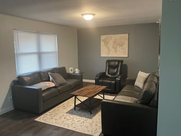 A living room with a black leather sofa, a leather recliner, a wooden coffee table, and a world map on the wall.