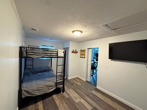 Une chambre avec un lit superposé, un téléviseur à écran plat fixé au mur et une porte donnant sur une autre pièce.