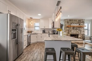 Une cuisine moderne dotée d’un grand îlot central, d’appareils électroménagers en acier inoxydable et d’un mur décoratif en pierre.
