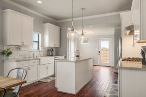 Une cuisine moderne avec des meubles blancs, un îlot central, des luminaires suspendus et une vue sur l’extérieur.