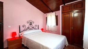 Un dormitorio con cama, mesita de noche, lámpara roja, armario de madera y ventana con cortinas.
