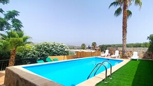 A rectangular swimming pool with a clear blue water, surrounded by a stone wall, and a grassy area with white lounge chairs. - Country House 'Cucazorra' with Mountain View, Wi-Fi and Air Conditioning (Málaga)