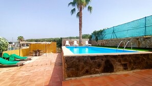 Une piscine avec des murs en pierre, un palmier et des chaises longues.