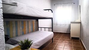 A small, compact room with a bunk bed, a single bed, a small table with a plant, a cabinet, and a window with curtains. - Country House 'Cucazorra' with Mountain View, Wi-Fi and Air Conditioning (Málaga)