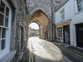 A narrow street with stone buildings, an archway, and a double yellow line road.
