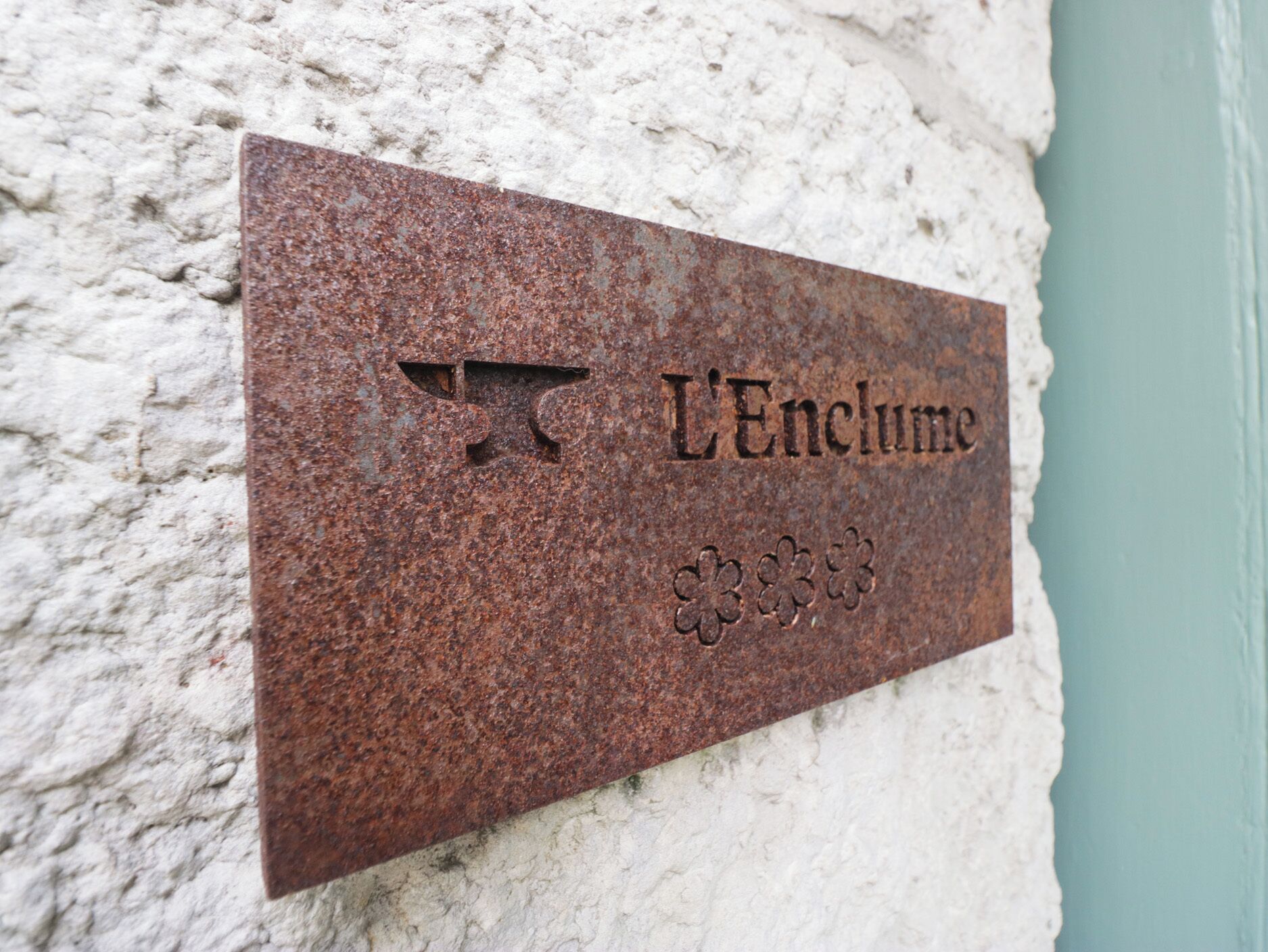 Uma placa de metal com a inscrição 'L'Enclume' numa parede texturizada.