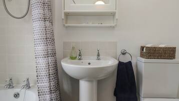 Un baño con un lavamanos blanco, dos grifos, una ducha con cortina de lunares, un espejo y una pequeña repisa con artículos de aseo.