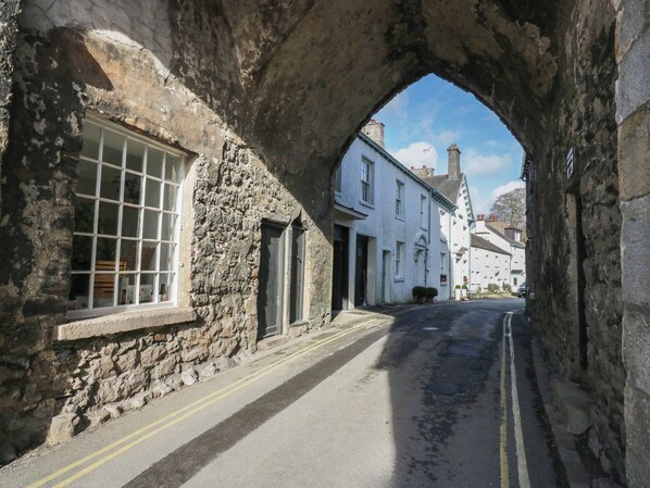 A narrow street with stone buildings, a visible window with a grid pattern, and a clear sky. - Flat 4 Tower House (Grange-over-Sands)