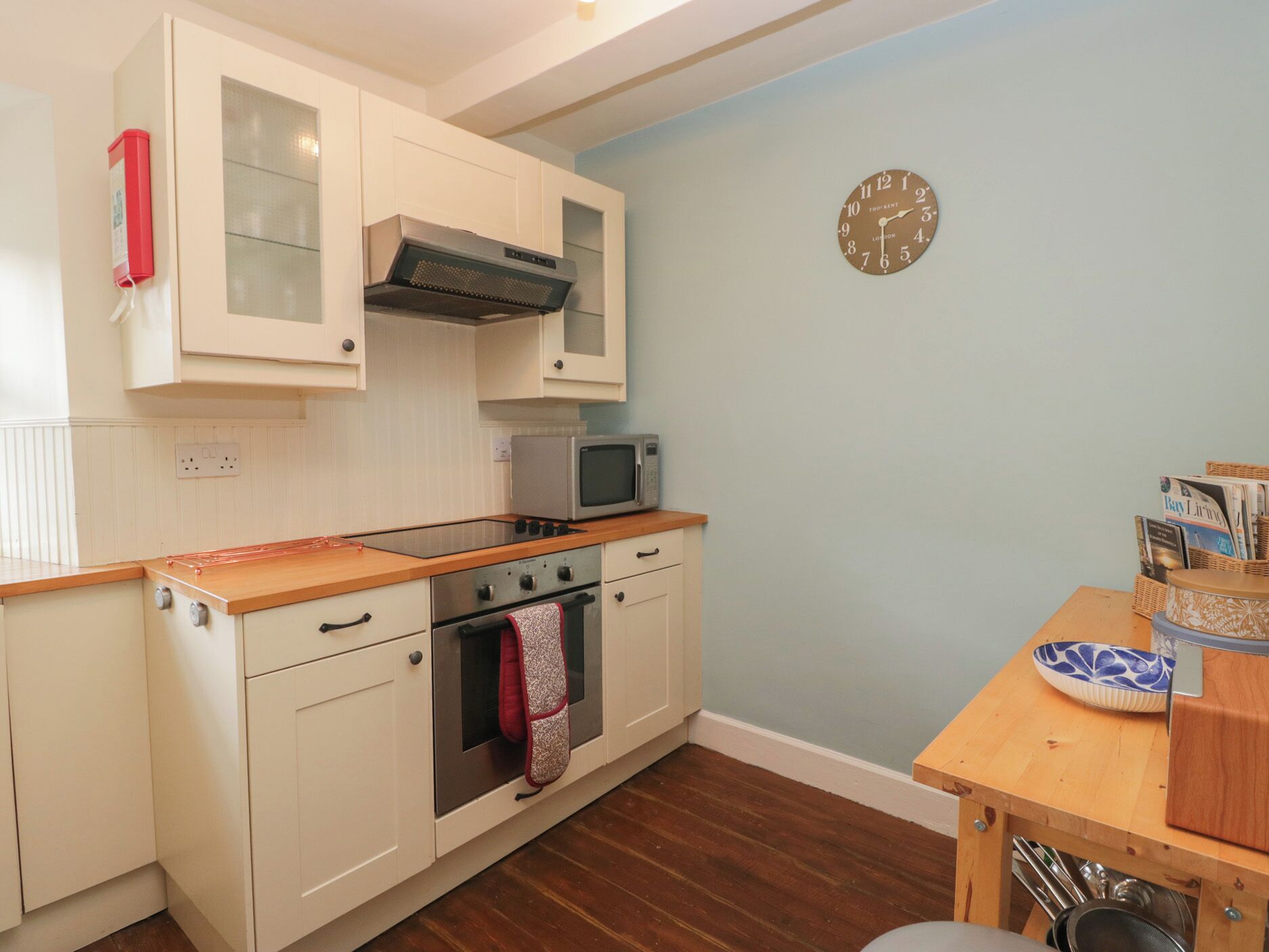 A compact kitchen with white cabinetry, a microwave, a stove, and a clock on the wall.