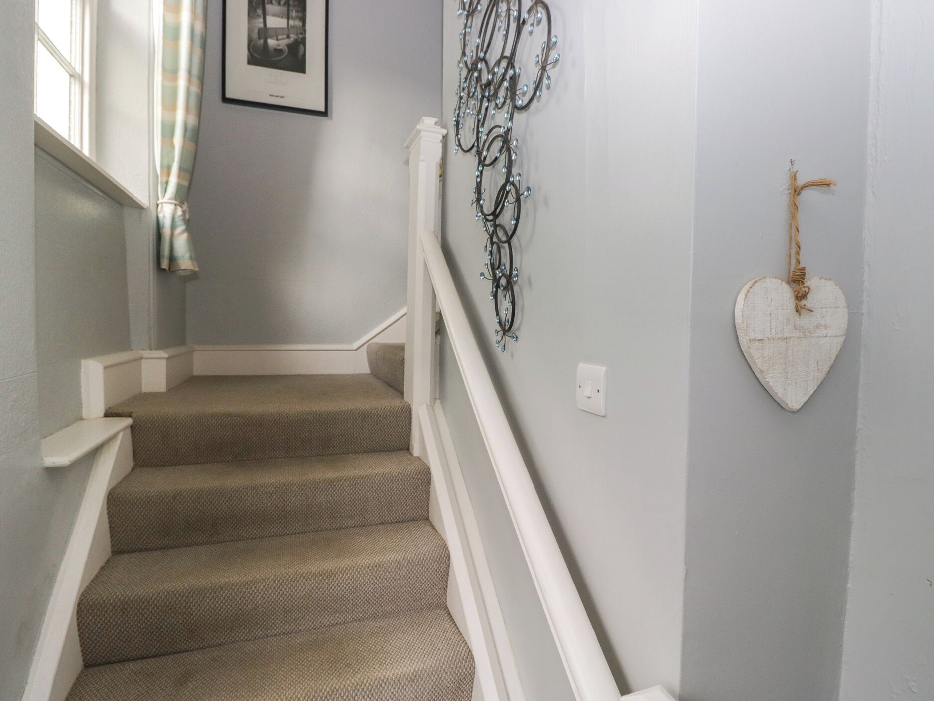 A staircase with beige carpeted steps and white railings, a wall-mounted light fixture, and a heart-shaped decoration.
