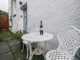 A white outdoor seating area with a round table and two chairs, a bottle of wine, and a glass.