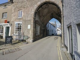 A street with a stone archway, buildings on either side, and a sign indicating the opening hours of a local business.
