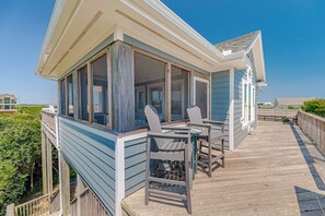 Ein Küstenhaus mit überdachter Veranda, zwei Adirondack-Stühlen und Blick auf den Ozean.