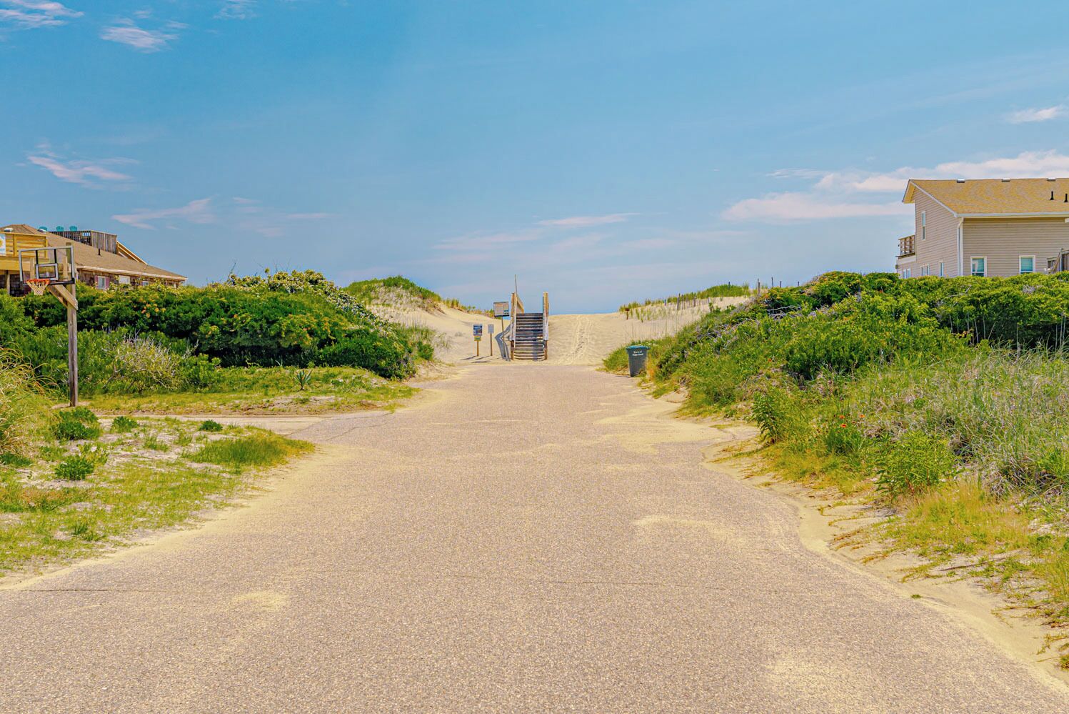 Ein asphaltierter Weg führt zu einem Strand, entlang dessen sich Häuser befinden.