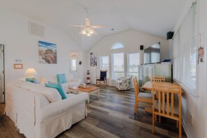 Ein geräumiges Wohnzimmer mit einem weißen Sofa, einem Holztisch, einem Esstisch mit Stühlen und einem Deckenventilator.