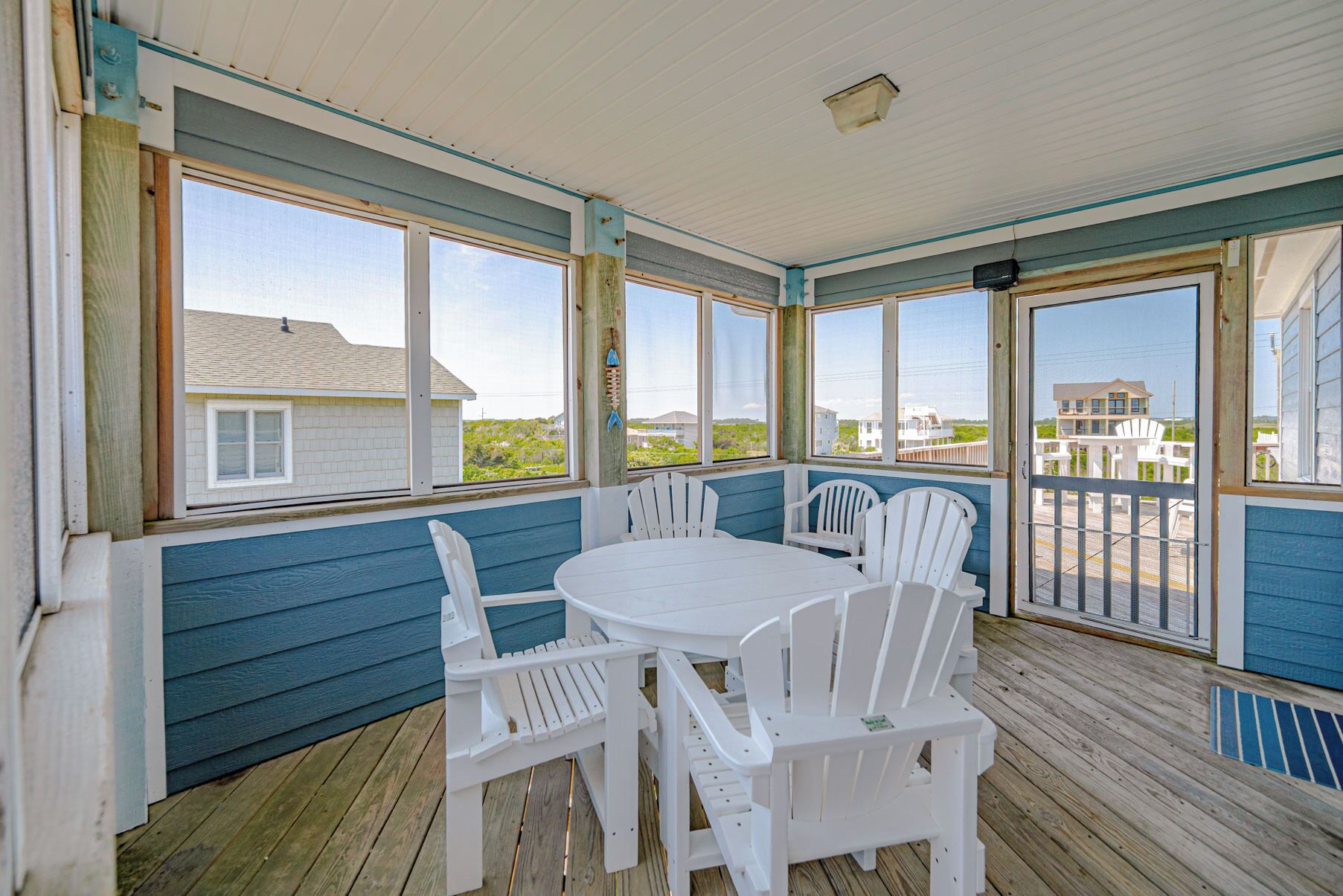 A covered outdoor seating area with a table and chairs, large windows, and a view of the beach.