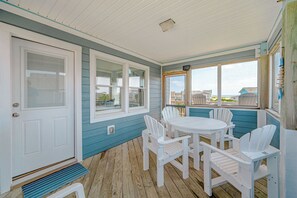 Eine überdachte Veranda mit einem weißen Tisch und Stühlen, einer Tür und Fenstern mit Jalousien.