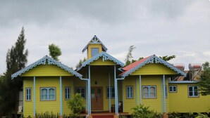 Una casa amarilla con techo rojo y detalles blancos, y un porche.