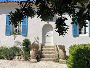 A building with a white facade, blue shutters, a white door, stone steps, and potted plants. - Family home of 150m2 with swimming pool in Hyères (Hyères)