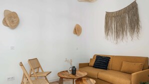 Una sala de estar con un sofá marrón, dos sillas de madera, una mesita de madera y un taburete redondo de madera.
