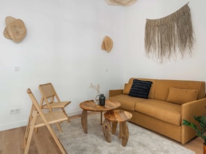 A living room with a brown sofa, two wooden chairs, a small wooden table, and a round wooden stool. - A modern, renovated apartment near Metro Line 2 (Paris)