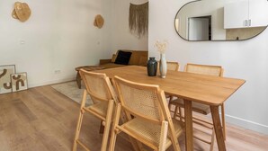 Un comedor con una mesa y sillas de madera, un jarrón con flores secas y un espejo en la pared.