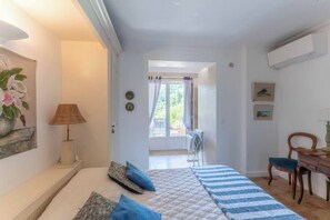 Une chambre à coucher avec un lit, un bureau et une chaise. Il y a une fenêtre avec des rideaux et une vue sur la verdure à l’extérieur.
