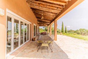 Une terrasse couverte avec une table et des chaises, des portes vitrées donnant sur un espace extérieur et une vue sur le paysage.