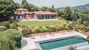 Una amplia casa con piscina, rodeada de exuberante vegetación y colinas.