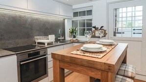 Een moderne keuken met een houten eettafel, een inbouwoven en een groot raam voor natuurlijk licht.