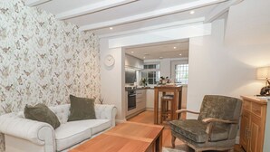Een moderne woonkamer met een witte bank, een houten salontafel en een grijze fauteuil. Achtergrond is een keuken zichtbaar met een bar.