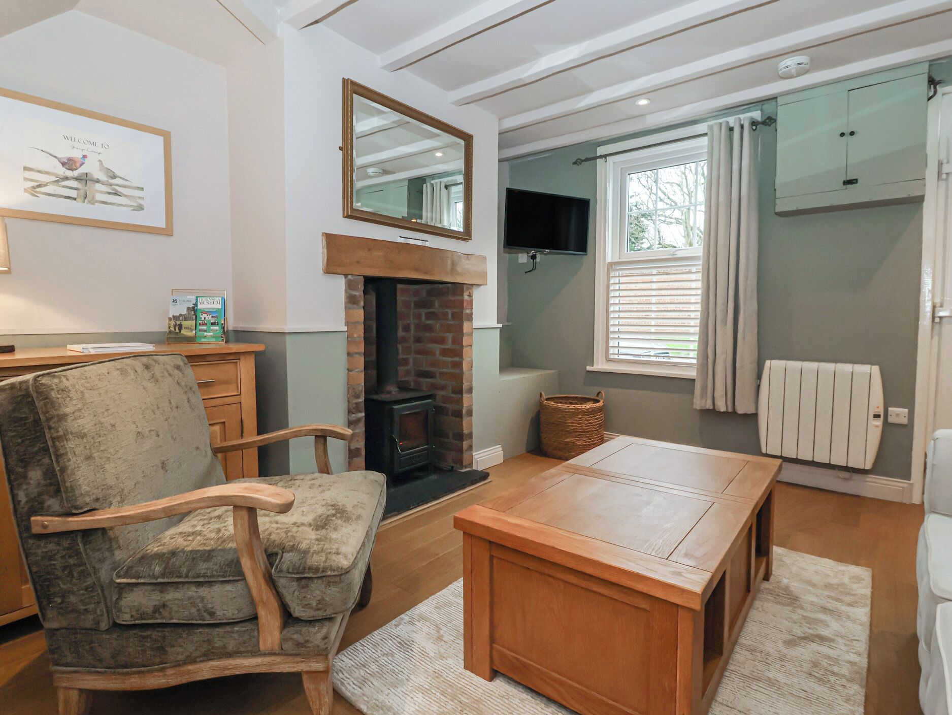 A cozy living room with a fireplace, a comfortable armchair, a wooden table, and a television mounted on the wall.