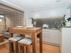 Eine moderne Küche mit weißen Schränken, einem Holztisch mit zwei Stühlen und einer Kücheninsel mit Spüle und Arbeitsplatte.