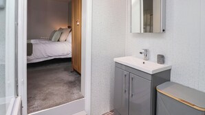 Een slaapkamer met een bed, een badkamer met een wastafel en spiegel, en een deur naar een andere kamer.