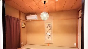 Ett traditionellt japanskt rum med tatamimattor på golvet, en hängande, sfärisk lampa och ett inramat konstverk på väggen.