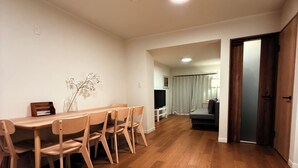 Ett rymligt vardagsrum med ett matbord och stolar i trä, en platt-TV och en soffa i mörk färg.