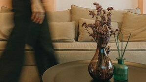Een woonkamer met een beige bank, een ronde salontafel en een vaas met gedroogde bloemen.