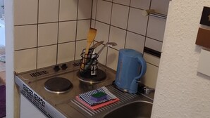 Kompakti keittiö, jossa on sisäänrakennettu astianpesukone, pesuallas ja sininen vedenkeitin.
