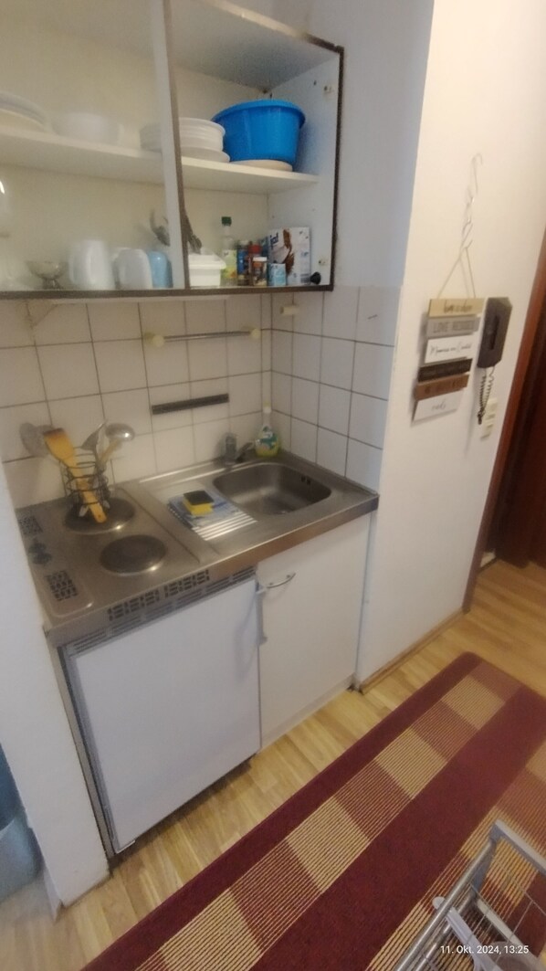 A small kitchen with a sink, a stove, and a mirror above the counter. There is a shelf with dishes and a blue container. - Apartment at the University of Mainz (Mainz)