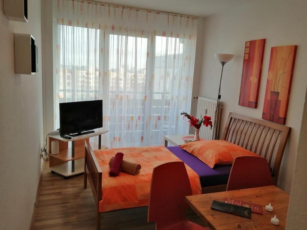 Ein Hotelzimmer mit zwei Betten, einem Fernseher, einem Tisch mit einem Buch und einer Vase mit Blumen.