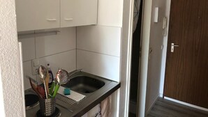 Pieni keittiö, jossa on valkoiset kaapit, ruostumattomasta teräksestä valmistettu pesuallas ja puinen ovi.