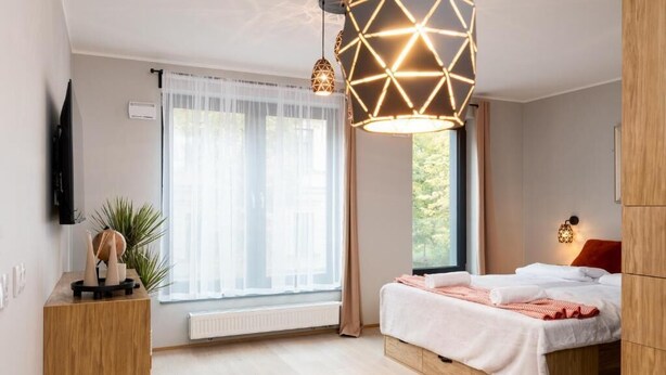 A modern bedroom with a bed, bedside table, and a large window. - Malila Apartments Cracow Grzegórzecka 15 (Kraków)