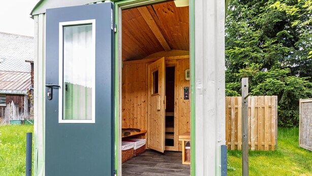 Une petite cabane en bois, dont la porte est ouverte, laissant entrevoir un espace de repos avec un banc et une petite table.