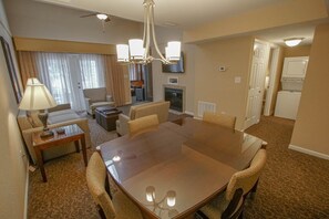 Habitación de hotel con mesa de comedor, sillas, sofá, lámpara, chimenea y televisor.