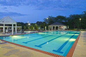 A swimming pool with a pavilion and a covered area, surrounded by trees and a well-lit walkway.