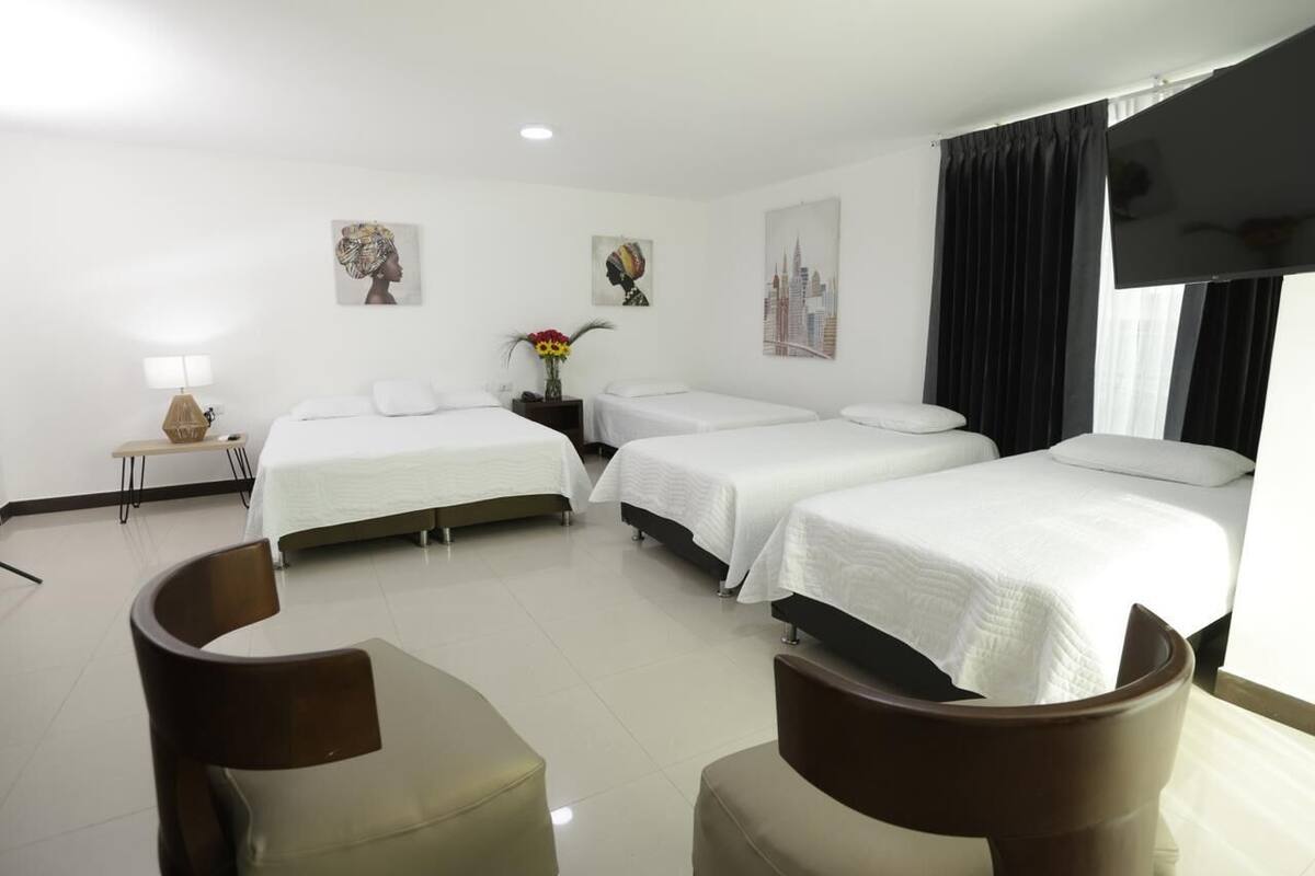 Une chambre d’hôtel avec trois lits simples, un téléviseur à écran plat, une petite table avec une lampe et des œuvres d’art accrochées aux murs.