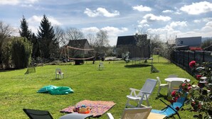 A grassy backyard with outdoor furniture, a volleyball net, and a trampoline. - Large family home in the heart of Redon near the train station (Redon)