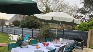 A neatly set outdoor dining area with a table covered by a white tablecloth, surrounded by green chairs, and shaded by a large umbrella. - Large family home in the heart of Redon near the train station (Redon)